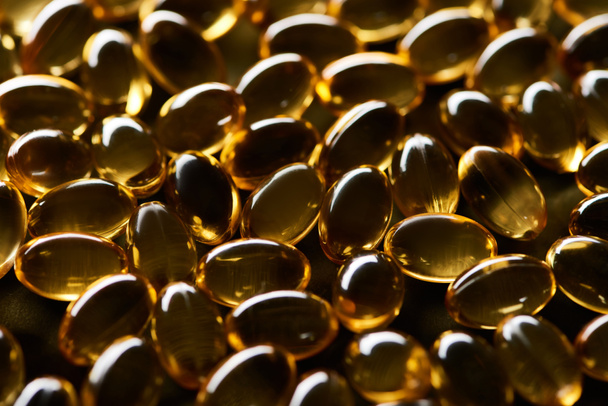 close up view of shiny golden fish oil capsules on black background in dark - Photo, Image