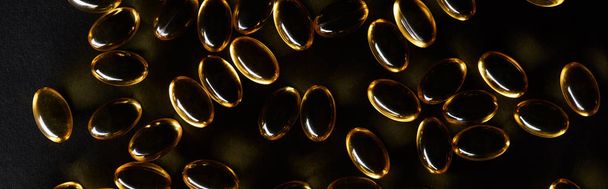 top view of golden fish oil capsules on black background in dark, panoramic shot - Foto, Imagen