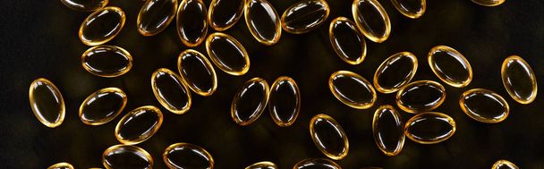 top view of golden fish oil capsules on black background in dark, panoramic shot - Foto, Imagem