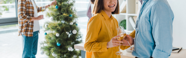 İş adamı ve mutlu iş kadınının iş arkadaşlarının ve Noel ağacının yanında şampanya bardaklarını tokuşturuşunun panoramik görüntüsü.  - Fotoğraf, Görsel