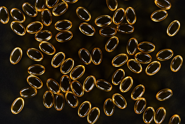Koyu arkaplanda altın balık yağı kapsüllerinin üst görüntüsü - Fotoğraf, Görsel