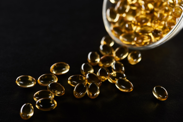 selective focus of golden fish oil capsules in glass bowl isolated on black - Foto, afbeelding