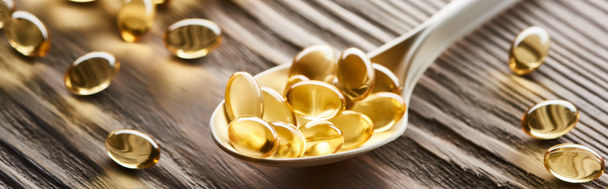 gouden visolie capsules in lepel op houten tafel, panoramisch schot - Foto, afbeelding