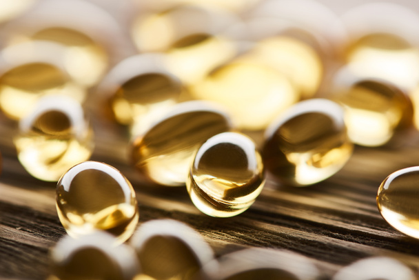 close-up zicht op gouden visolie capsules verspreid over houten tafel - Foto, afbeelding