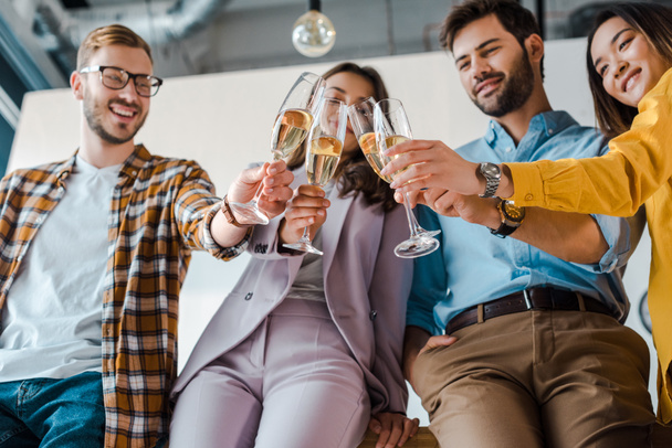 vista de ángulo bajo de hombres de negocios alegres y mujeres de negocios multiculturales brindar copas de champán en la oficina
  - Foto, Imagen