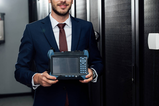 cropped view of happy businessman holding reflectometer in server room  - Photo, Image