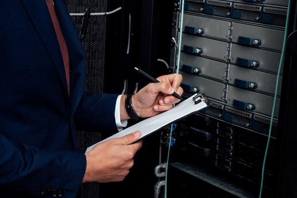 cropped view of man in suit holding clipboard and pen in data center  - 写真・画像
