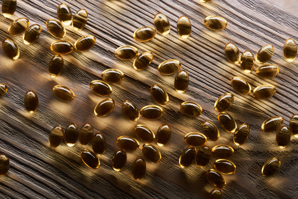 glanzende gouden visolie capsules verspreid over houten tafel - Foto, afbeelding
