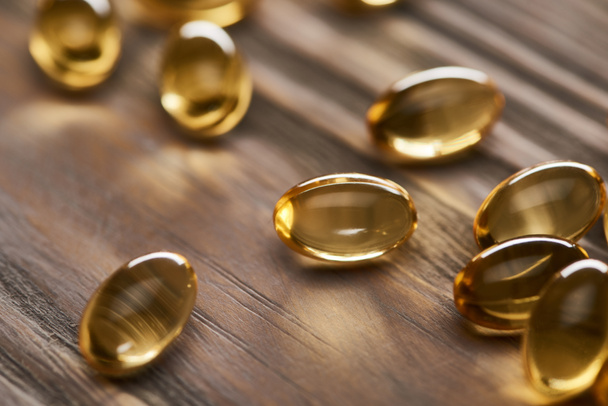 close up view of shiny golden fish oil capsules scattered on wooden table - Photo, Image