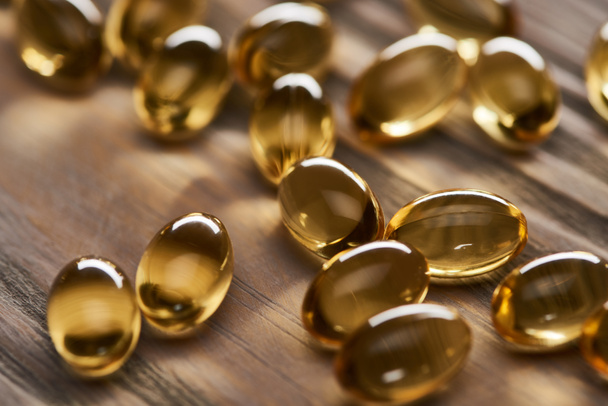 close-up zicht op glanzende gouden visolie capsules verspreid over houten tafel - Foto, afbeelding