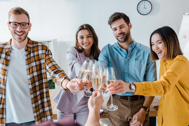 bijgesneden beeld van de man toasten champagne glazen met vrolijke zakenmannen en multiculturele zakenvrouwen in het kantoor  - Foto, afbeelding