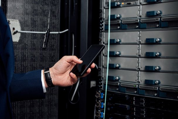 cropped view of man holding smartphone with blank screen in server room  - Photo, Image
