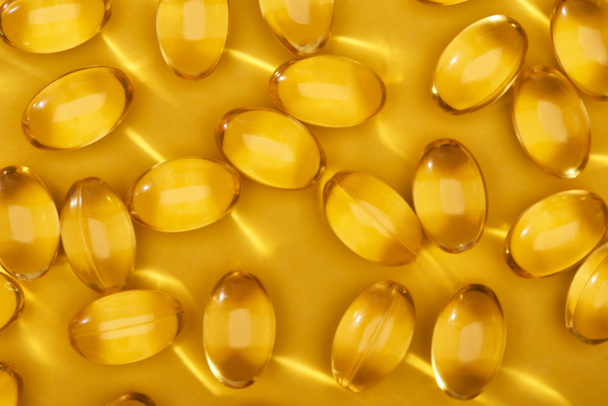 widok z góry złote błyszczące kapsułki oleju rybnego rozrzucone na żółtym jasnym tle - Zdjęcie, obraz