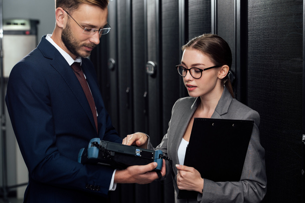 handsome businessman in glasses holding reflectometer near businesswoman in data center  - Photo, Image