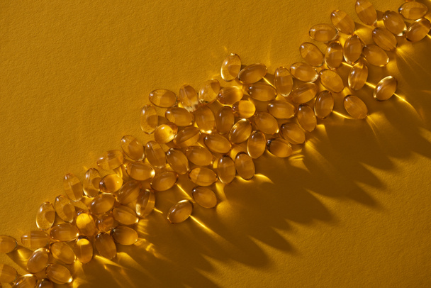 top view of golden shiny fish oil capsules on yellow background in dark - Photo, Image