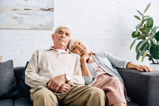 mąż i uśmiechnięta żona leżący na ramieniu i siedzący na kanapie w mieszkaniu  - Zdjęcie, obraz