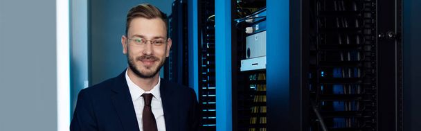 panoramic shot of businessman in glasses smiling in data center  - Photo, Image