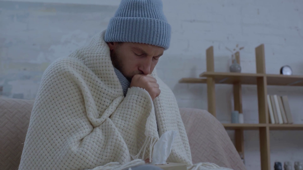 nemocný muž v teplém klobouku kašlání a kýchání při balení do přikrývky - Záběry, video
