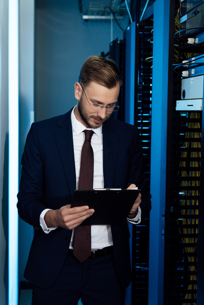 handsome businessman in glasses holding clipboard in data center  - Photo, Image