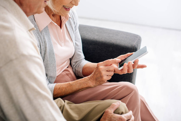 cropped view of husband and wife using smartphone in apartment  - Fotoğraf, Görsel