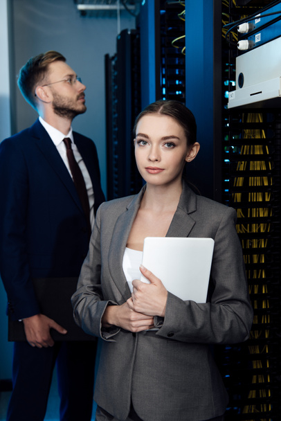 selective focus of attractive businesswoman holding digital tablet near bearded businessman in data center  - Photo, Image