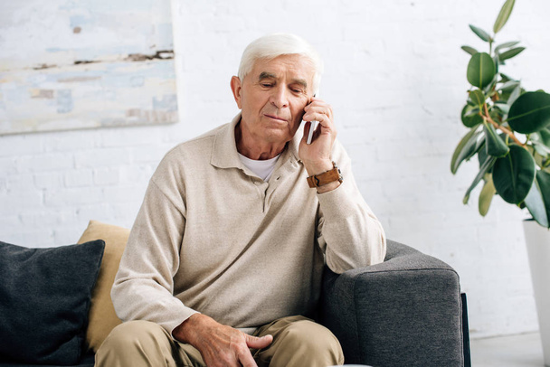 Senior sitzt auf Sofa und telefoniert in Wohnung mit Smartphone  - Foto, Bild