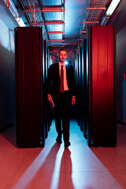bearded businessman in glasses holding digital tablet and walking in server room  - Photo, Image