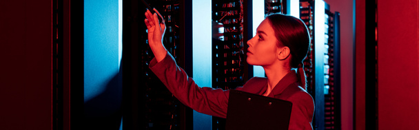 panoramic shot of businesswoman holding clipboard and looking at server room  - Photo, Image