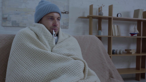 hombre enfermo en abrigo de sombrero caliente en manta y temperatura de medición
 - Imágenes, Vídeo