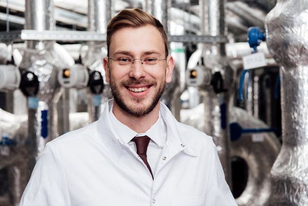 cheerful engineer in glasses and white coat looking at camera  - Photo, Image