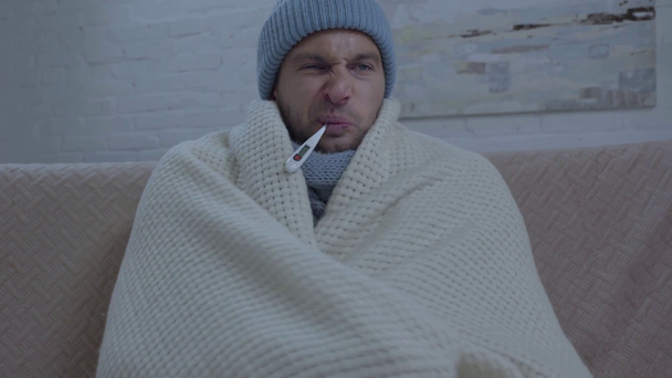 nemocný muž v teplém klobouku balení v přikrývce a měření teploty - Záběry, video