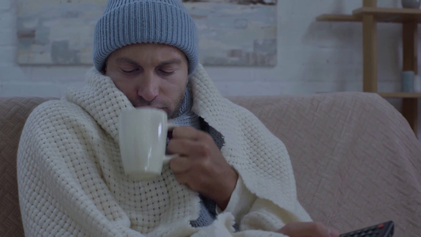 nemocný muž pití teplý nápoj a sledování televize - Záběry, video