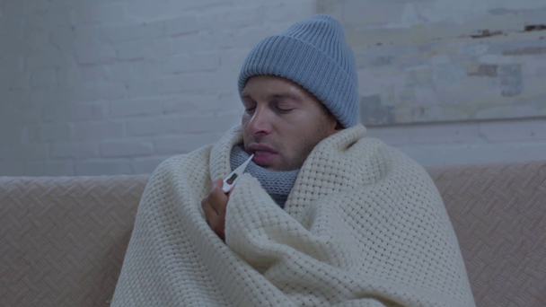 ill mean in warm hat wrapping in blanket and measuring temperature - Footage, Video