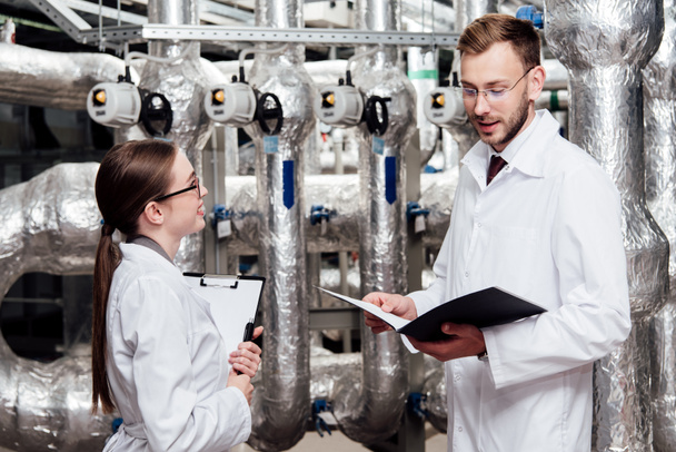 happy woman in white coat looking at handsome engineer with folder  - Photo, Image