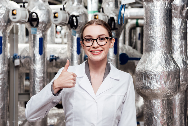 ingeniero feliz en bata blanca y gafas que muestran el pulgar hacia arriba cerca del sistema de aire comprimido
  - Foto, Imagen