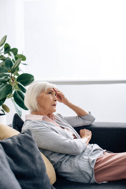 senior woman having headache and sitting on sofa in apartment  - Foto, immagini