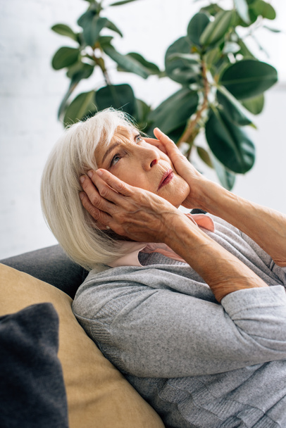 mujer mayor con dolor de cabeza y sentado en el sofá en el apartamento
  - Foto, Imagen