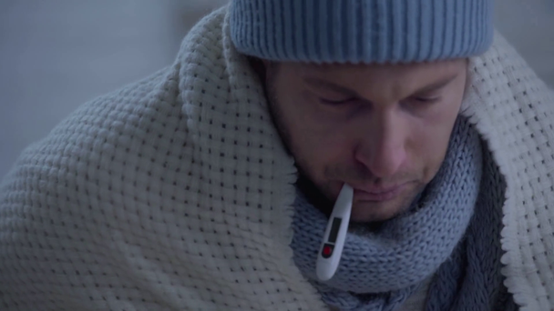 hombre grueso en abrigo de sombrero caliente en manta y temperatura de medición
 - Imágenes, Vídeo