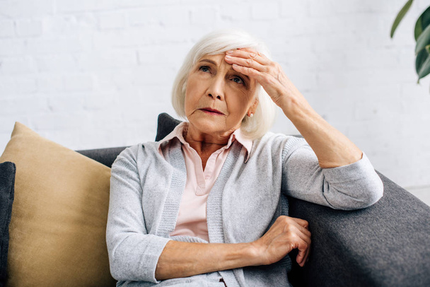 senior woman having headache and sitting on sofa in apartment  - Photo, image