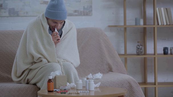 Sairas mies istuu lähellä pöytää lääkkeiden kanssa ja käyttää nenäsumutetta
 - Materiaali, video