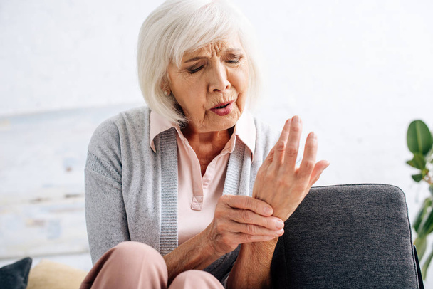 attraente donna anziana che ha l'artrite in mano in appartamento
  - Foto, immagini