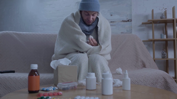 άρρωστος άνθρωπος φτερνίζεται ενώ κάθεται κοντά στο τραπέζι με τα φάρμακα  - Πλάνα, βίντεο