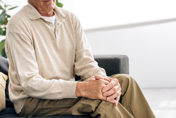 cropped view of senior man sitting on sofa and having knee Arthritis in apartment  - Photo, Image