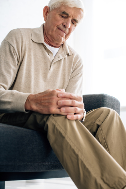 vista angolo basso di uomo anziano seduto sul divano e avendo l'artrite del ginocchio in appartamento
  - Foto, immagini