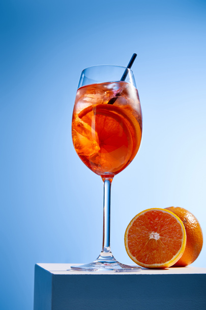 коктейль Aperol Spritz с соломой в стекле и апельсинами на синем фоне
  - Фото, изображение