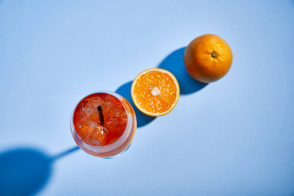 top view of cocktail Aperol Spritz with straw in glass and oranges on blue background  - Photo, Image