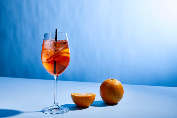 cocktail Aperol Spritz with straw in glass and oranges on blue background  - Foto, imagen