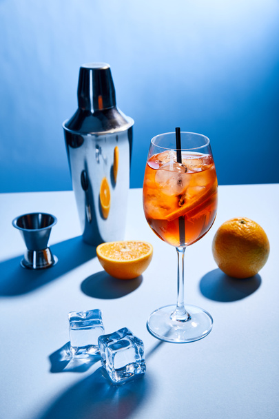 cocktail Aperol Spritz, laranjas, agitador, cubos de gelo e copo de medição no fundo azul
  - Foto, Imagem