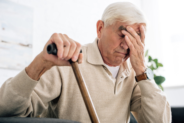 senior man with headache and holding wooden cane in apartment  - Photo, Image