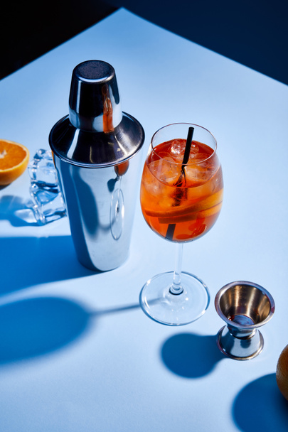 Aperol Spritz kokteylinin yüksek açılı görüntüsü, turuncu, titretici, buz küpleri ve mavi arkaplanda ölçüm kabı  - Fotoğraf, Görsel